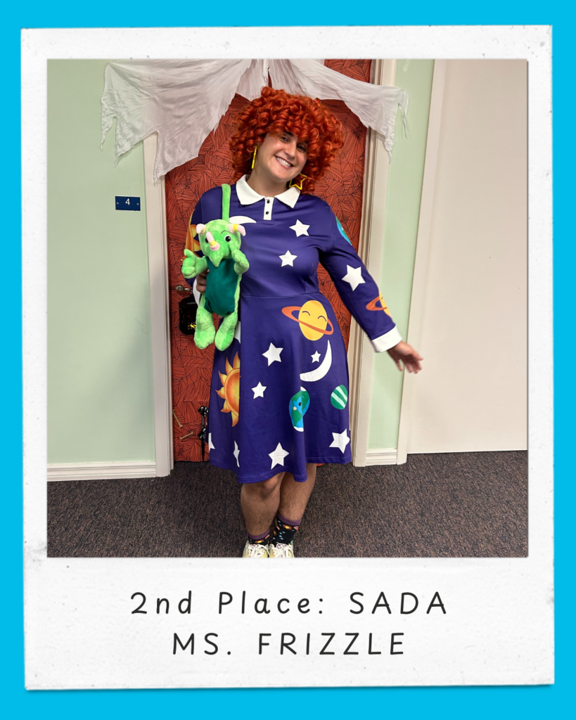 Sada dressed as Ms. Frizzle, a science teacher from the Magic School Bus.  She is wearing a very curly, short red wig, long sleeve purple dress with white stars, yellow moon, yellow sun and colorful planets sprinkled throughout, colorful black socks and white tennis shoes with rainbow colors.  She is holding the class pet, a green lizard named Liz. At the bottom of the image, there is a white frame with light blue edges, featuring the text: "2nd Place: Sada,
Ms. Frizzle"