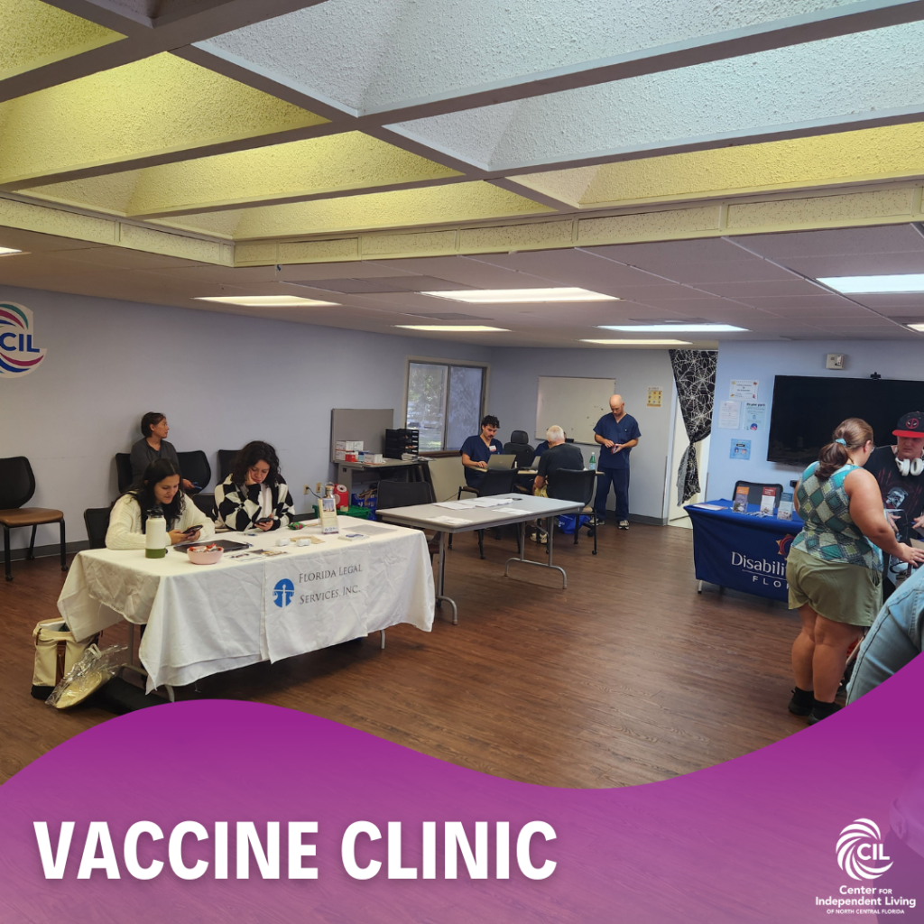 This image shows the vaccine clinic held indoors at the CIL Gainesville office, with tables and representatives from different organizations set up around the room. On the left, a table is labeled "Florida Legal Services, Inc." with two people sitting and working. To the right, a table with materials is labeled "Disability Rights Florida." Several individuals are standing or sitting in different areas of the room, engaging in conversations or activities. In the background, two healthcare professionals in blue scrubs are preparing or assisting at another station. The room has a clean and bright interior, with a light-colored ceiling and wooden floors. A purple banner across the bottom reads "Vaccine Clinic," accompanied by the Center for Independent Living (CIL) logo.