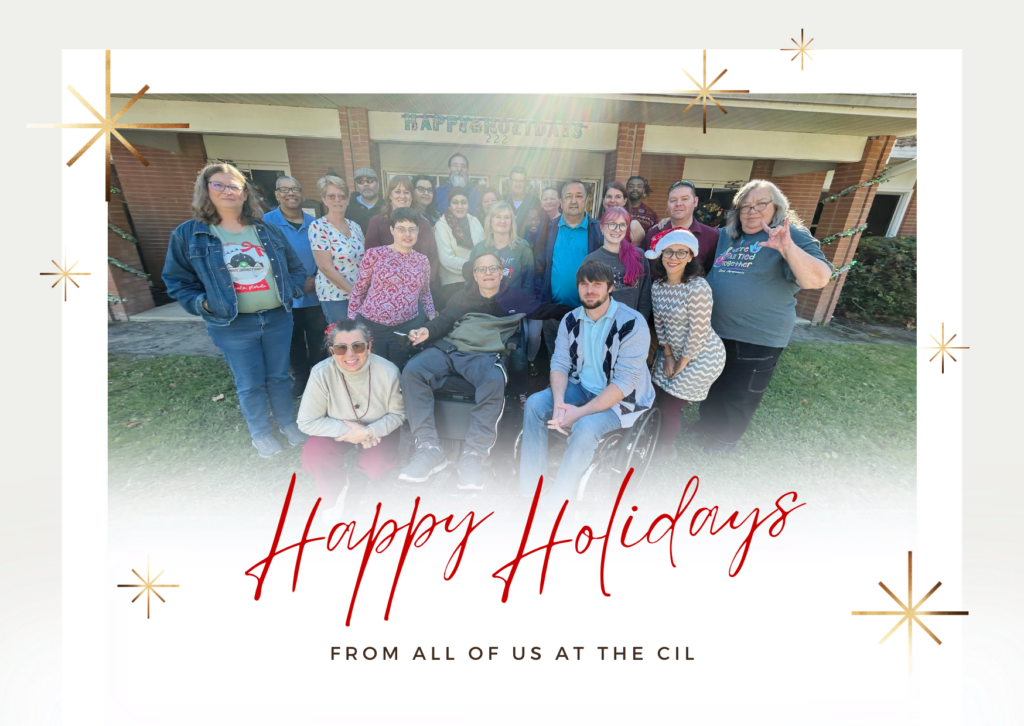 This is a holiday greeting card featuring a group photo of individuals posing outdoors in front of a brick building with a banner that reads "Happy Holidays." The group consists of diverse people, some standing and others sitting, including individuals in wheelchairs. The background shows a green lawn and part of the building’s porch. The card is framed with a festive design, including small gold and white starbursts, and features the text “Happy Holidays” in elegant red script, followed by “From All of Us at the CIL” in uppercase black letters beneath it. The overall tone of the card is cheerful and inclusive.