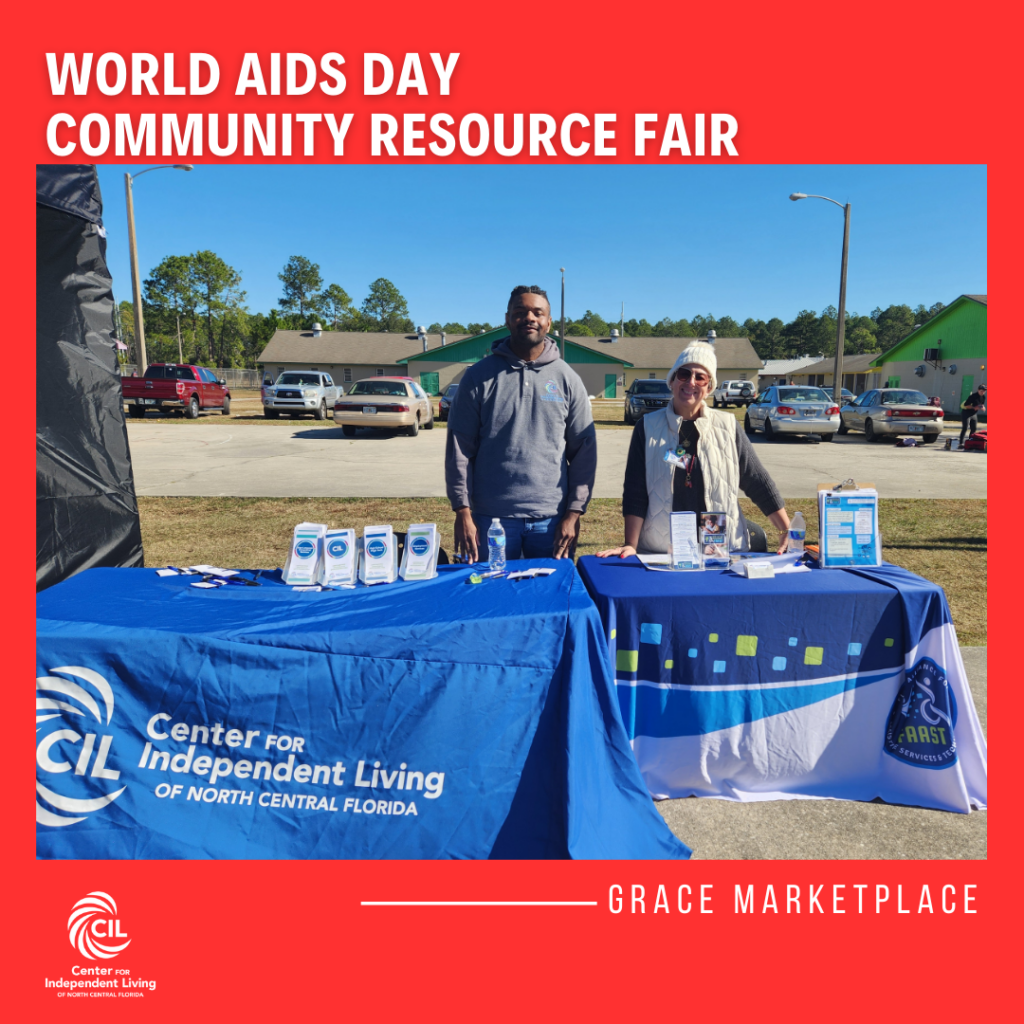 The image shows two individuals standing behind tables at the World AIDS Day Community Resource Fair at GRACE Marketplace. On the left is a man wearing a gray sweatshirt, and on the right is a woman wearing a white jacket and beanie. Both are standing next to informational tables displaying pamphlets and materials related to the Center for Independent Living (CIL) and FAAST (Florida Alliance for Assistive Services and Technology). The setting is outdoors with cars parked in the background. The sky is clear, and the atmosphere appears sunny but cool. The red text at the top of the image reads "WORLD AIDS DAY COMMUNITY RESOURCE FAIR" and at the bottom, it says "GRACE MARKETPLACE."