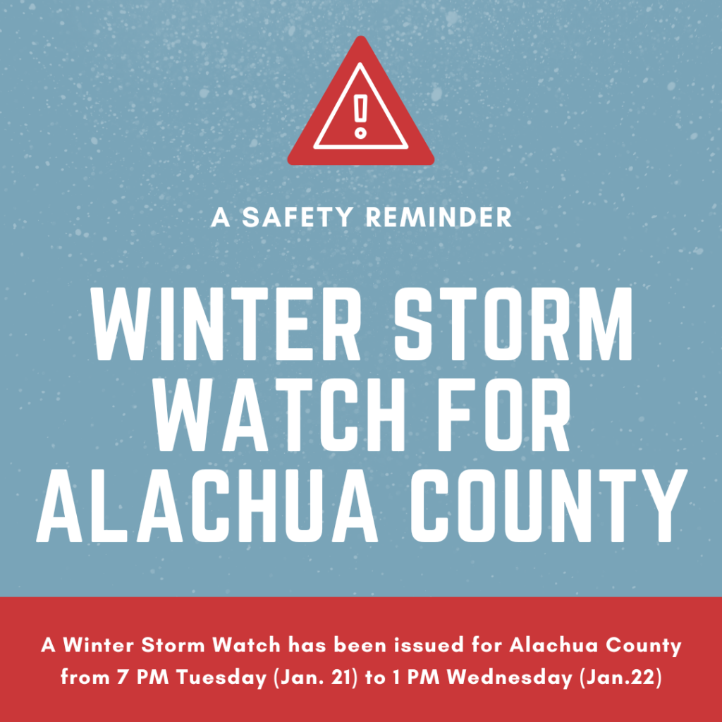 The image features a bold red triangle with an exclamation mark at the top, symbolizing a warning. Below this symbol, the text "A Safety Reminder" is displayed in a smaller font. The central text reads "WINTER STORM WATCH FOR ALACHUA COUNTY" in large, white letters. At the bottom of the image, a message reads: "A Winter Storm Watch has been issued for Alachua County from 7 PM Tuesday (Jan. 21) to 1 PM Wednesday (Jan. 22)." The background is a soft blue with a subtle snowflake pattern, and the text is framed by a red section at the bottom.