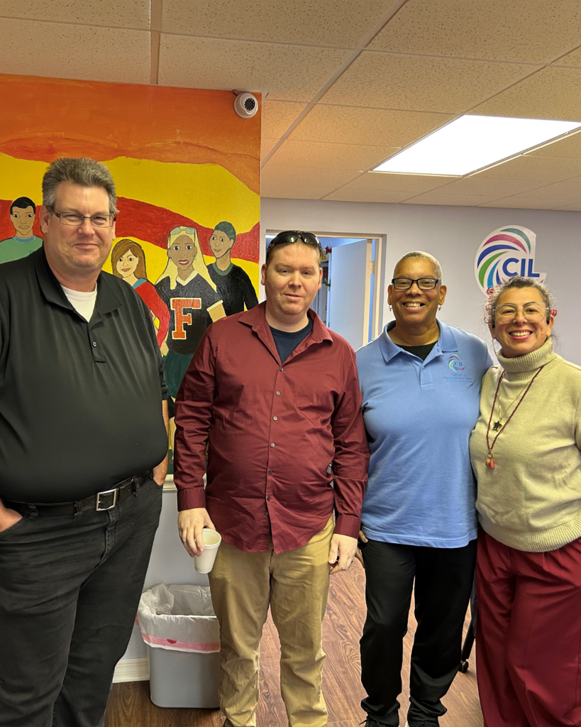 Four smiling people pose together in front of a colorful mural and a CIL logo, dressed in casual and business-casual attire.