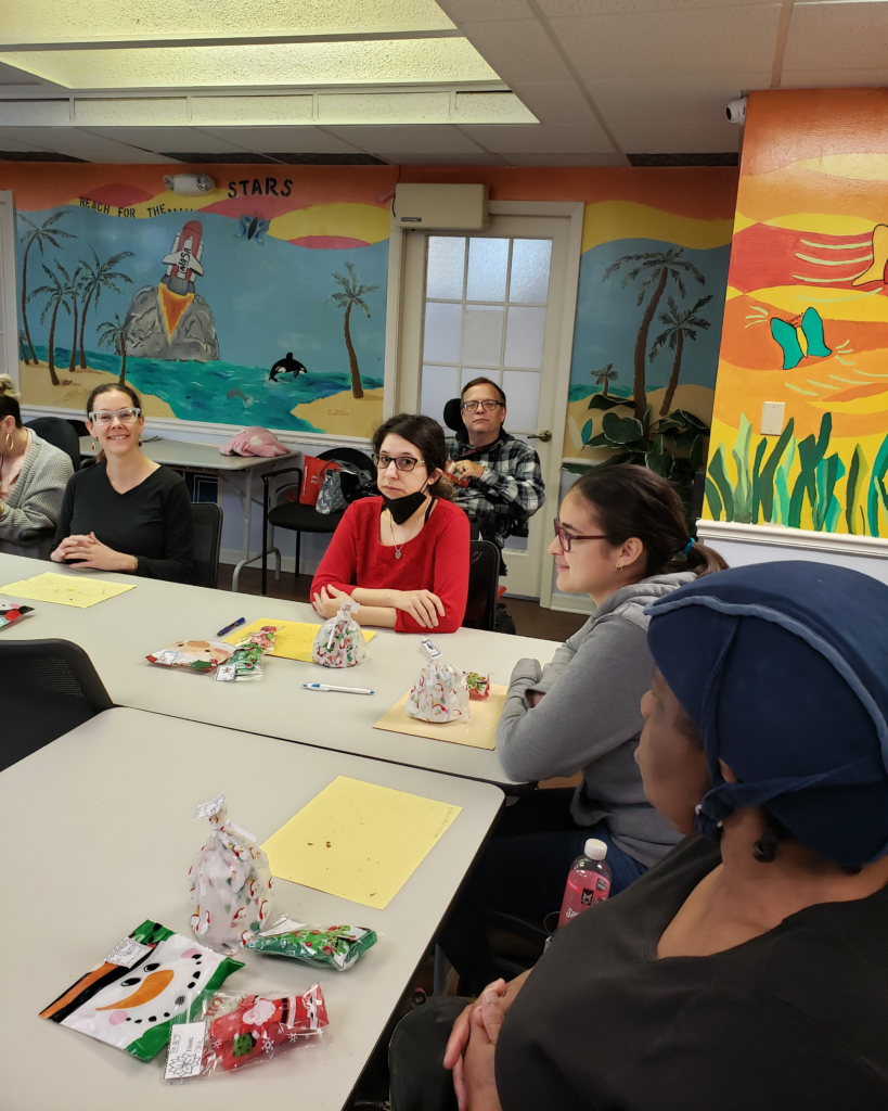 ILS participants gather at the Gainesville Holiday Party, sitting at a table with festive gift bags and crafting materials, surrounded by vibrant murals.