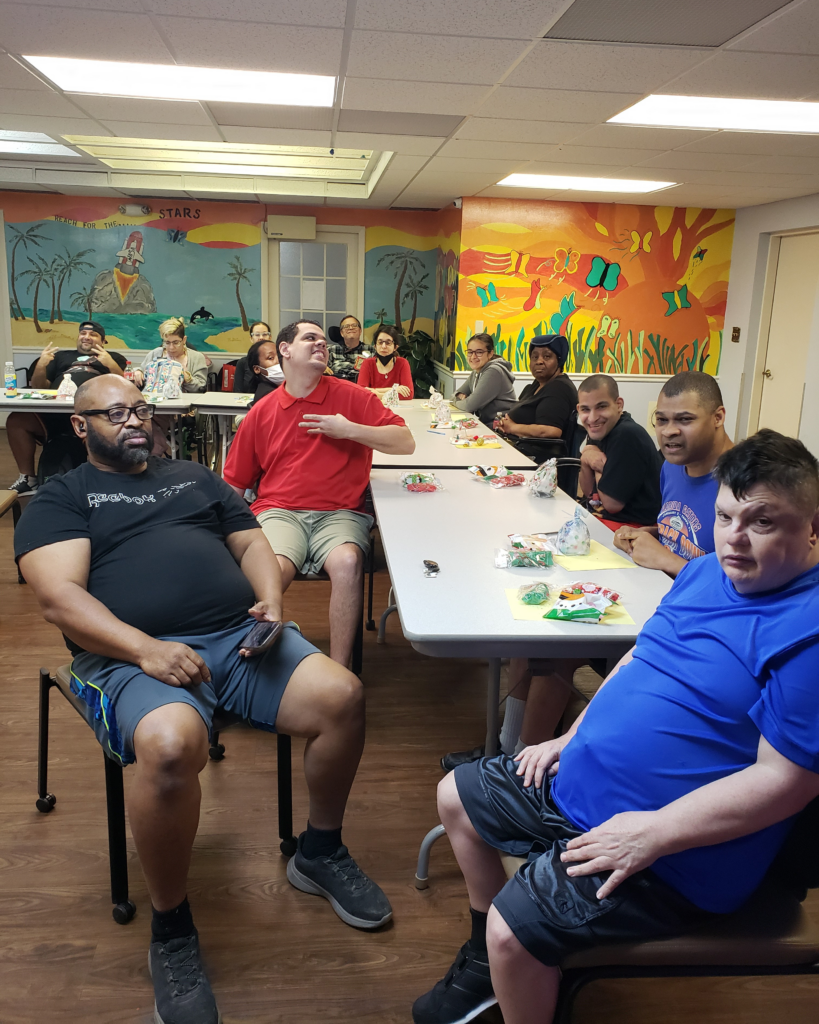 ILS participants at the Gainesville Holiday Party enjoy the event together, sitting at a table with gift bags and crafting materials in a colorful, festive room.