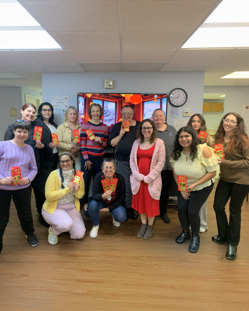 CIL staff are smiling and holding red envelopes in celebration of Lunar New Year, standing in front of a festive display with lanterns.