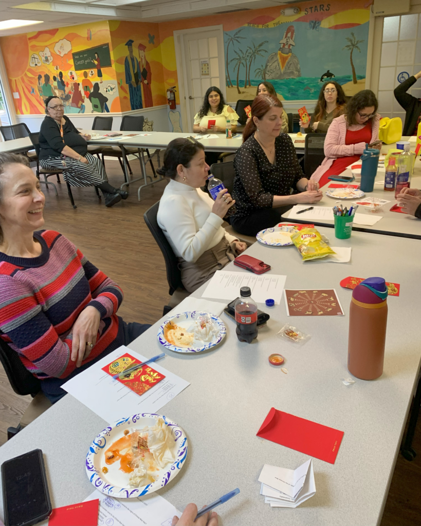 CIL staff gathered around tables at the center's Lunar New Year celebration, enjoying food, holding red envelopes, and engaging in activities together.